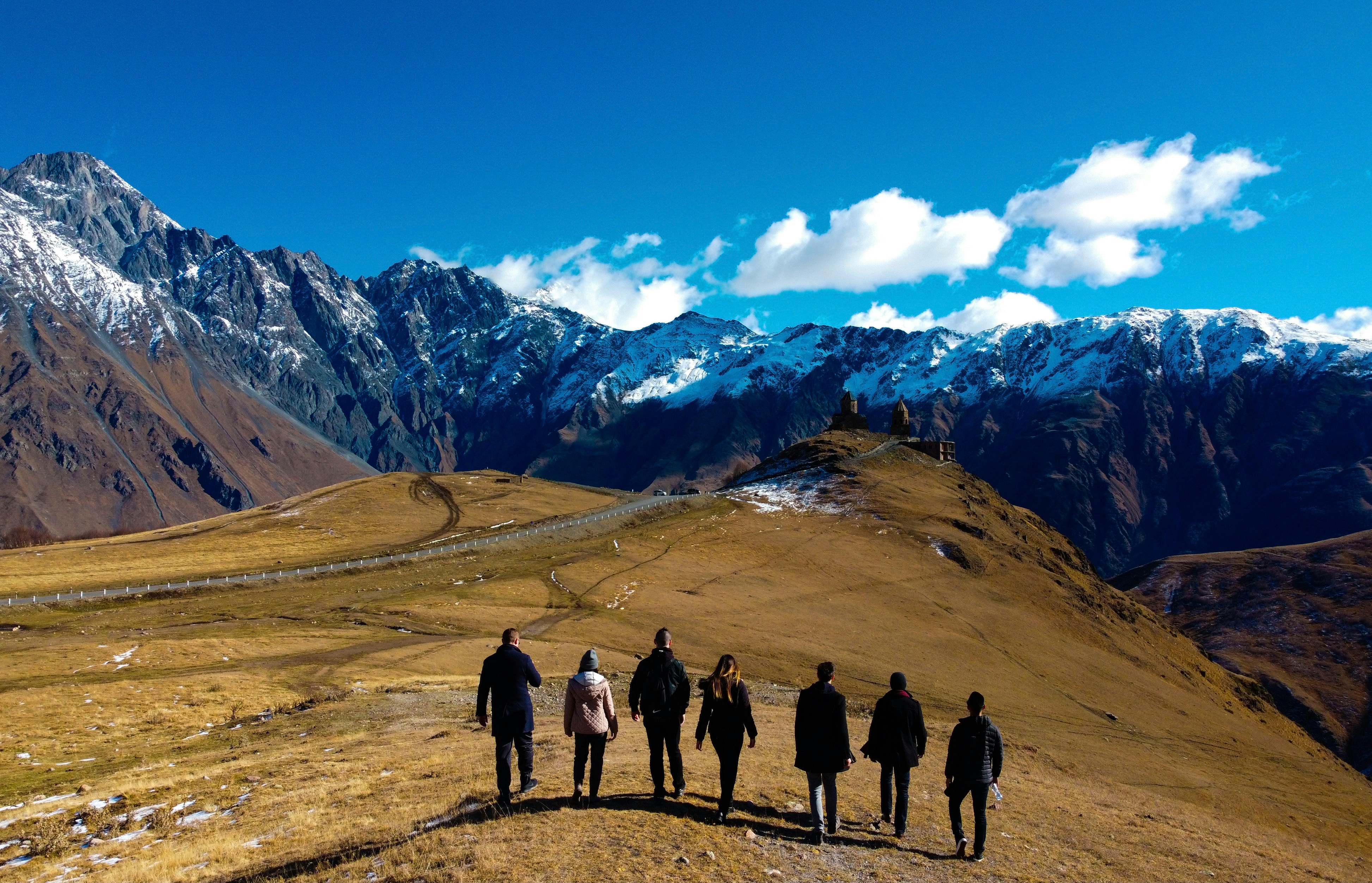 Photo by Unsplash An illustrative photo of a group of people standing on a brown field near a snow covered mountain.