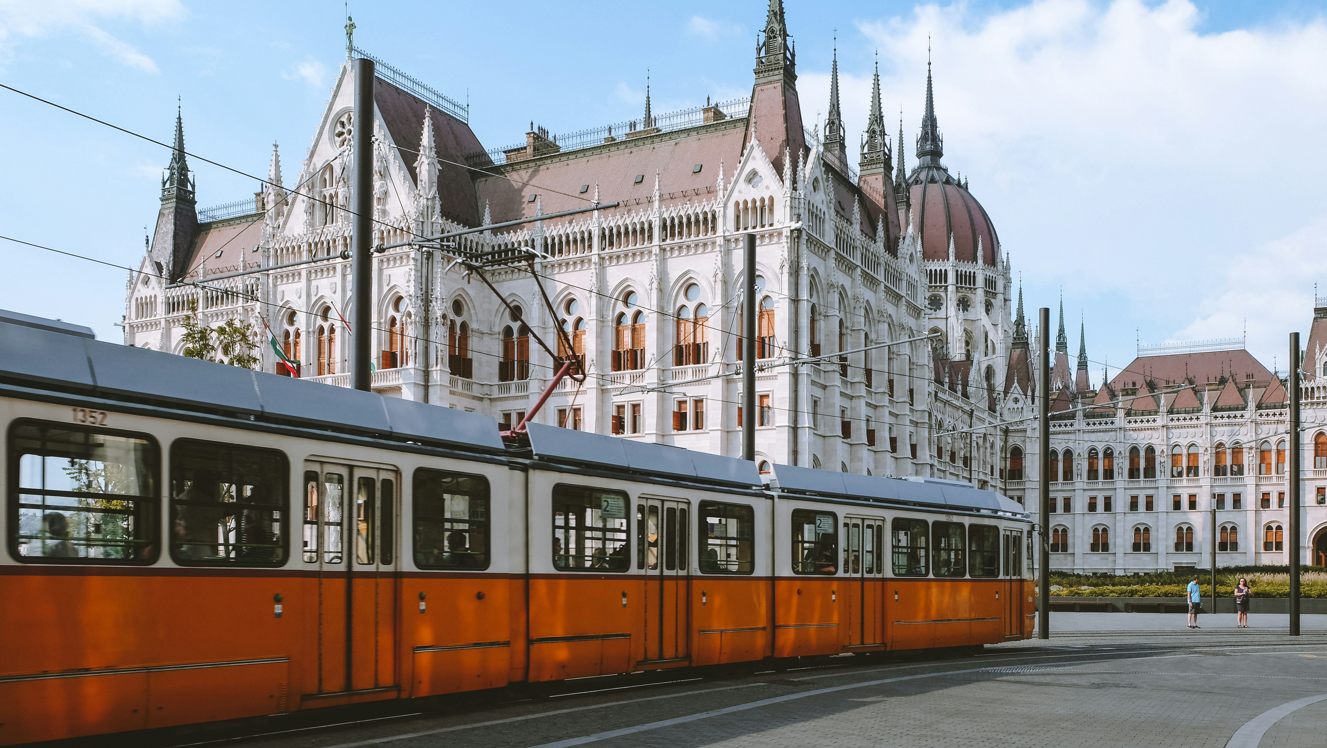Photo by Unsplash An illustrative photo of an orange and white tram near the Hungarian Parliament.