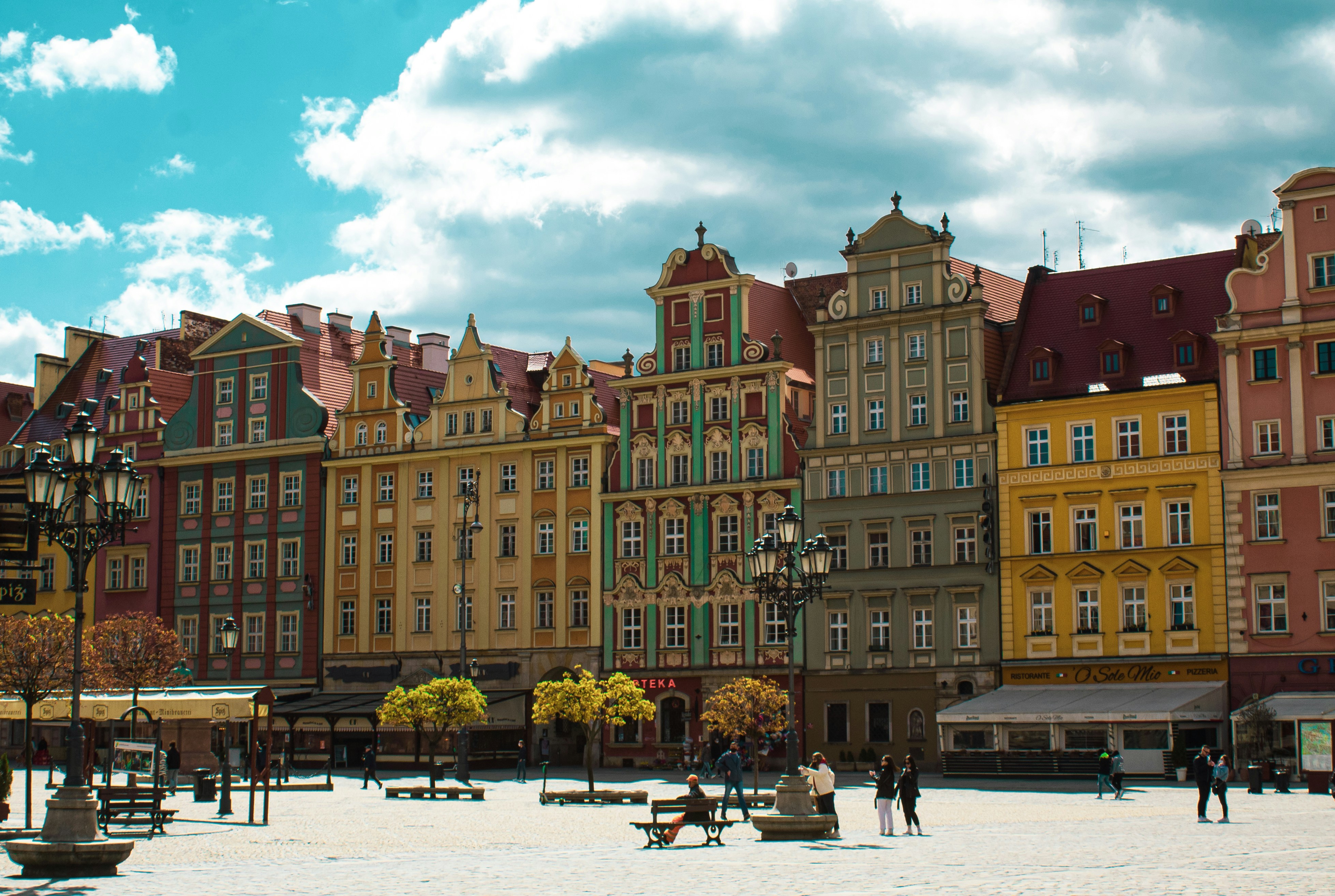 An illustrative photo of people walking near buildings of multiple colours.
