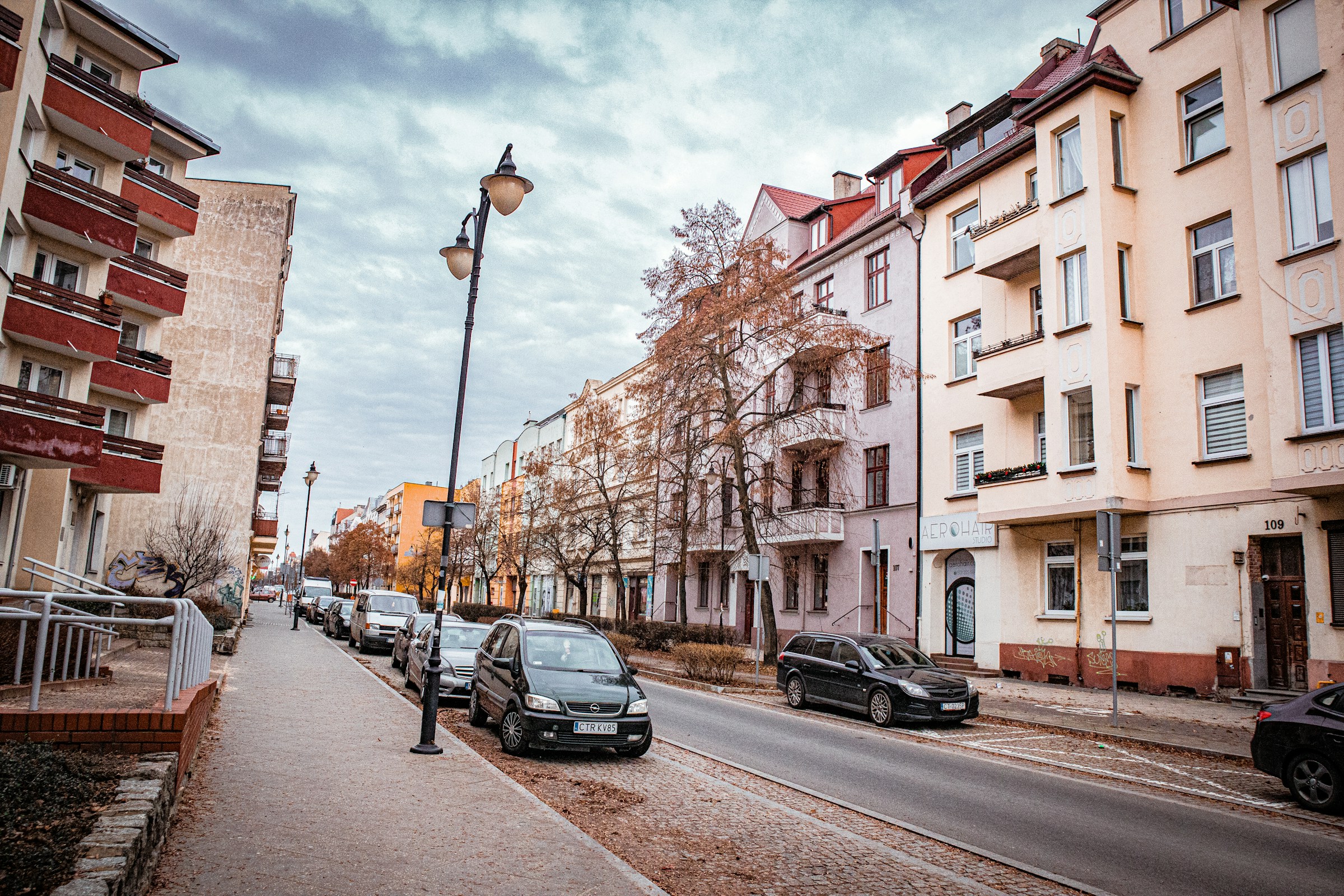 An illustrative photo of a street lined with parked cars next to tall buildings