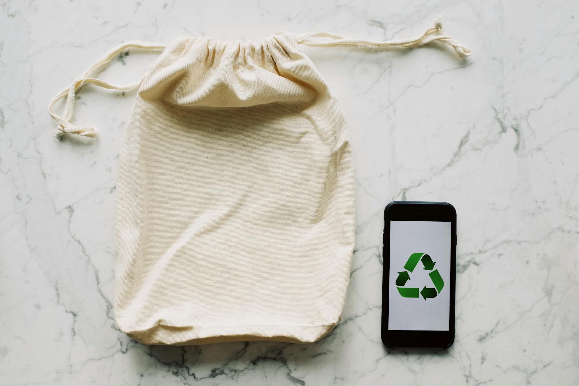 Reusable cloth bag beside a smartphone displaying a recycling symbol.