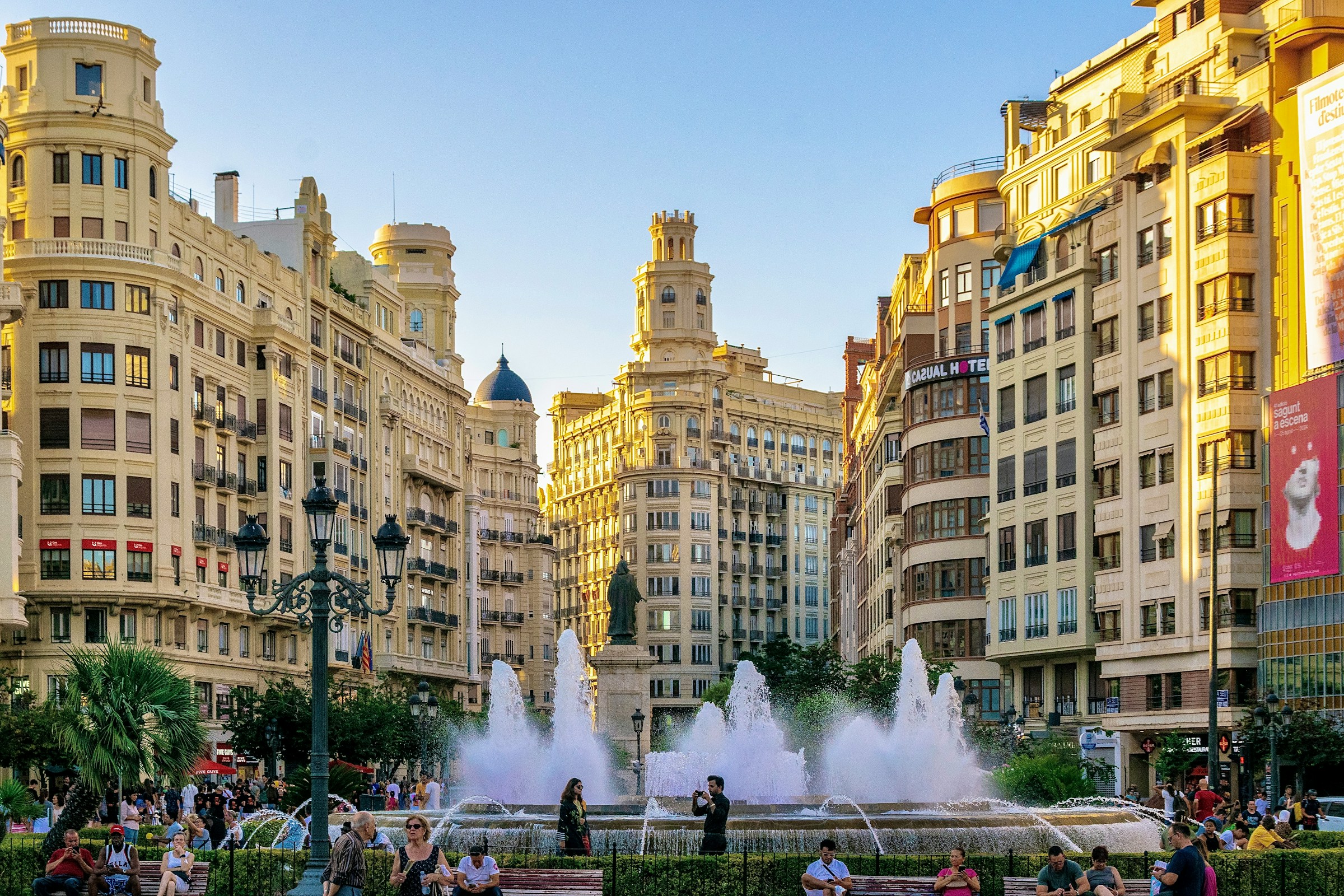 An illustrative photo of a group of people standing around a fountain in a city.