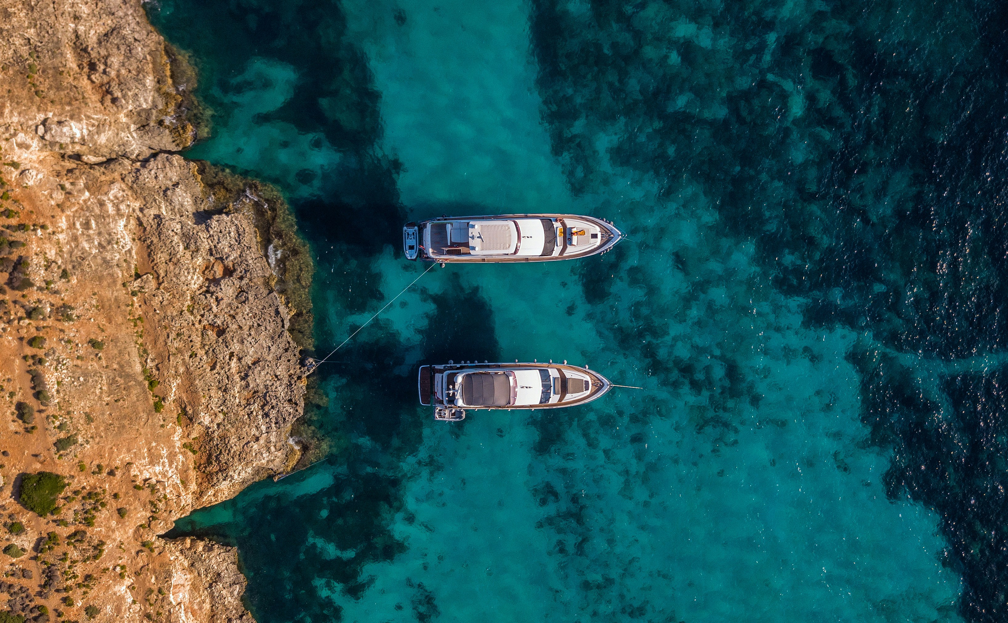 Photo by Unsplash An illustrative photo of two white boats in a body of water near a rocky shore.