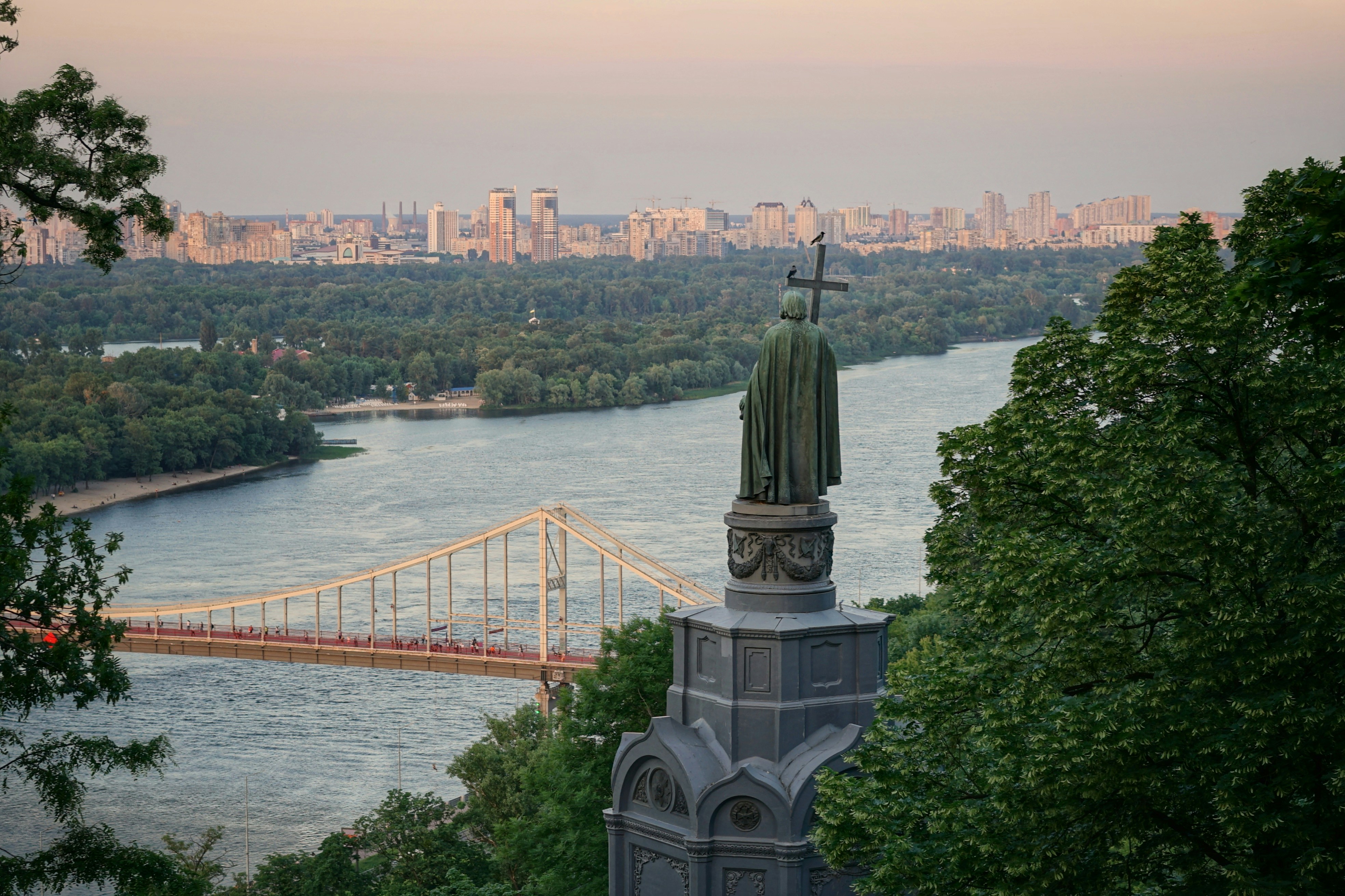 An illustrative photo of a statue by a bridge with a city in the background.
