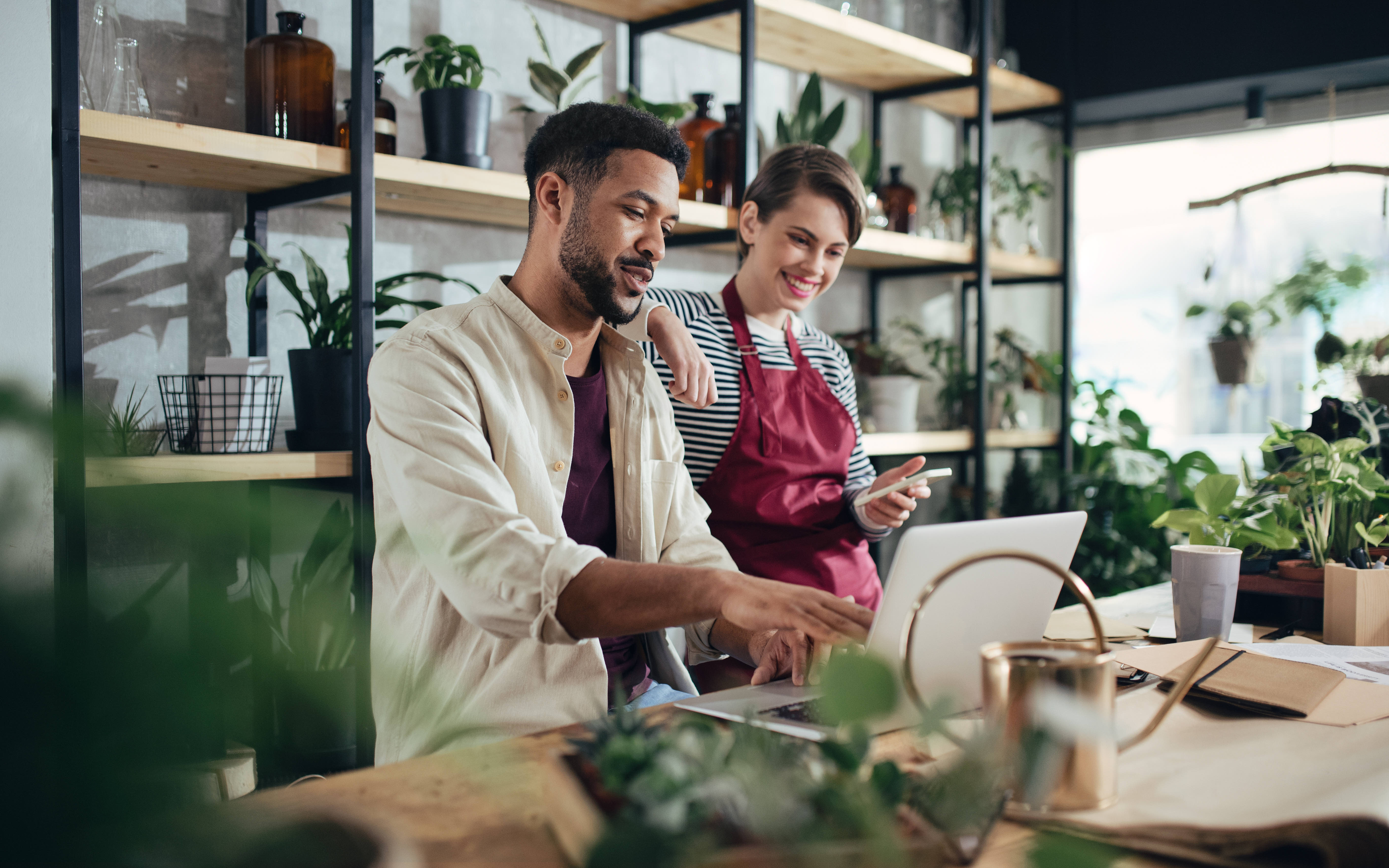 A photo presenting two people working together on a laptop in a plant-filled shop.
