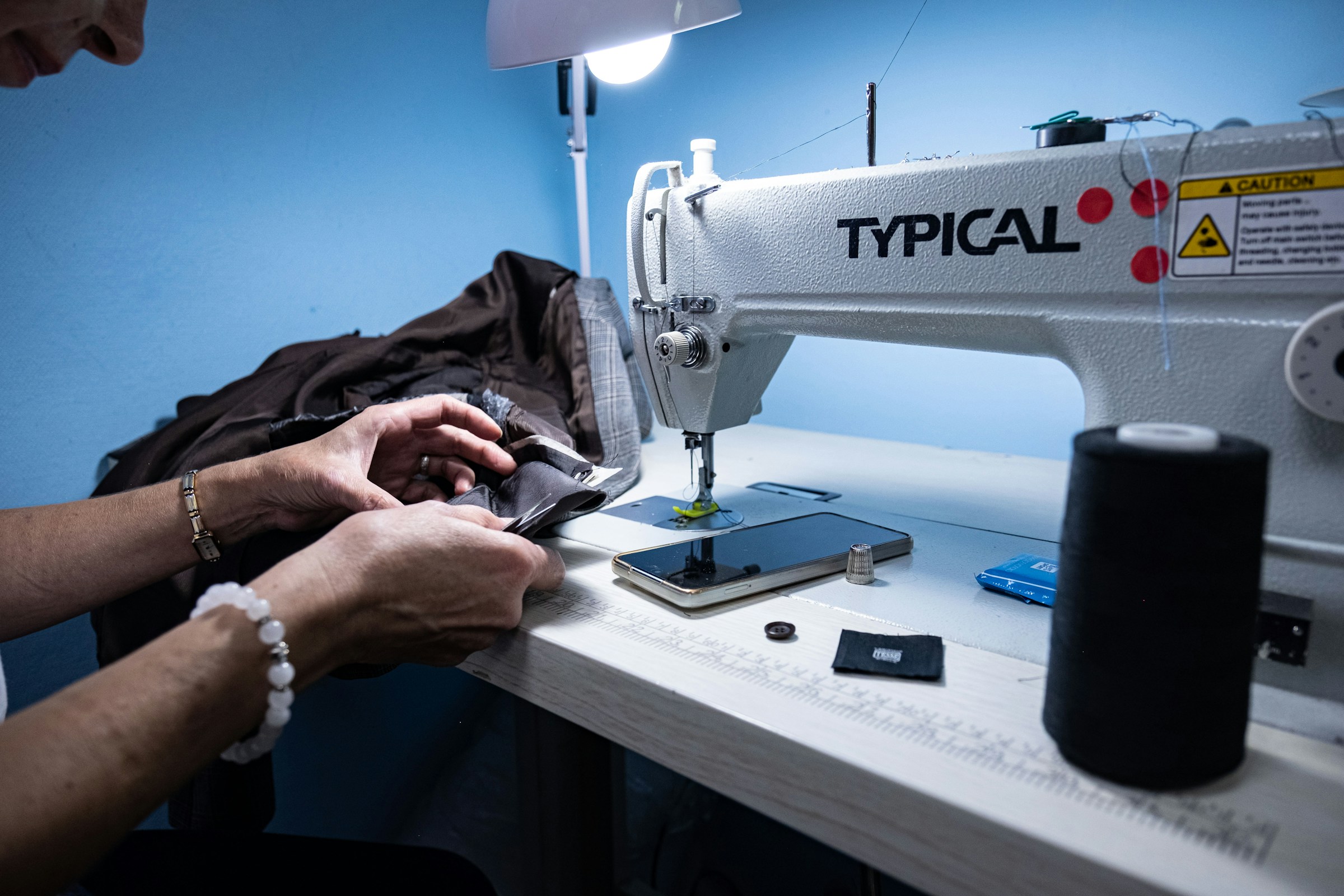 Person sewing fabric on an industrial sewing machine under a work lamp.