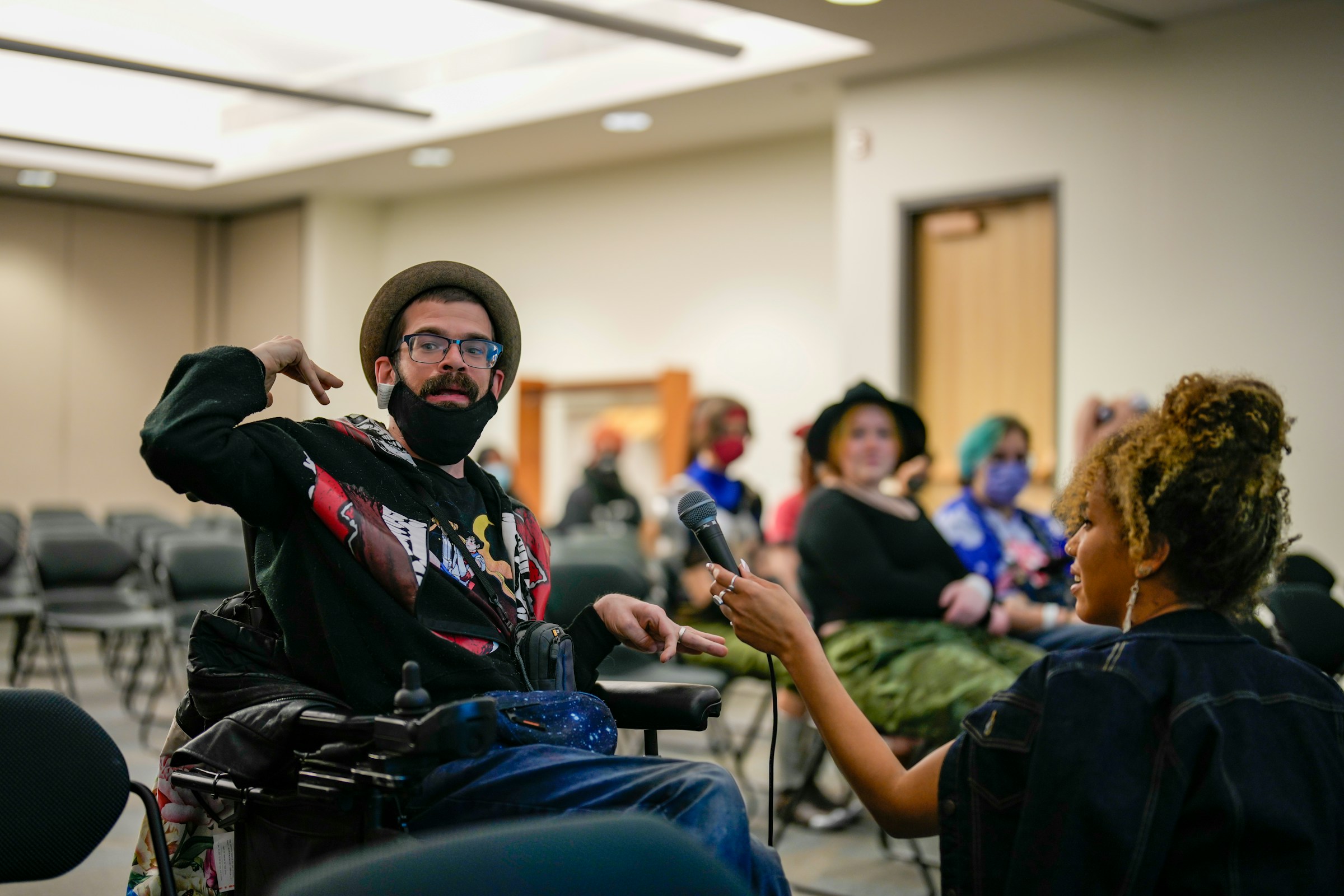 An illustrative photo of a person with disabilities sitting in a chair with a microphone.