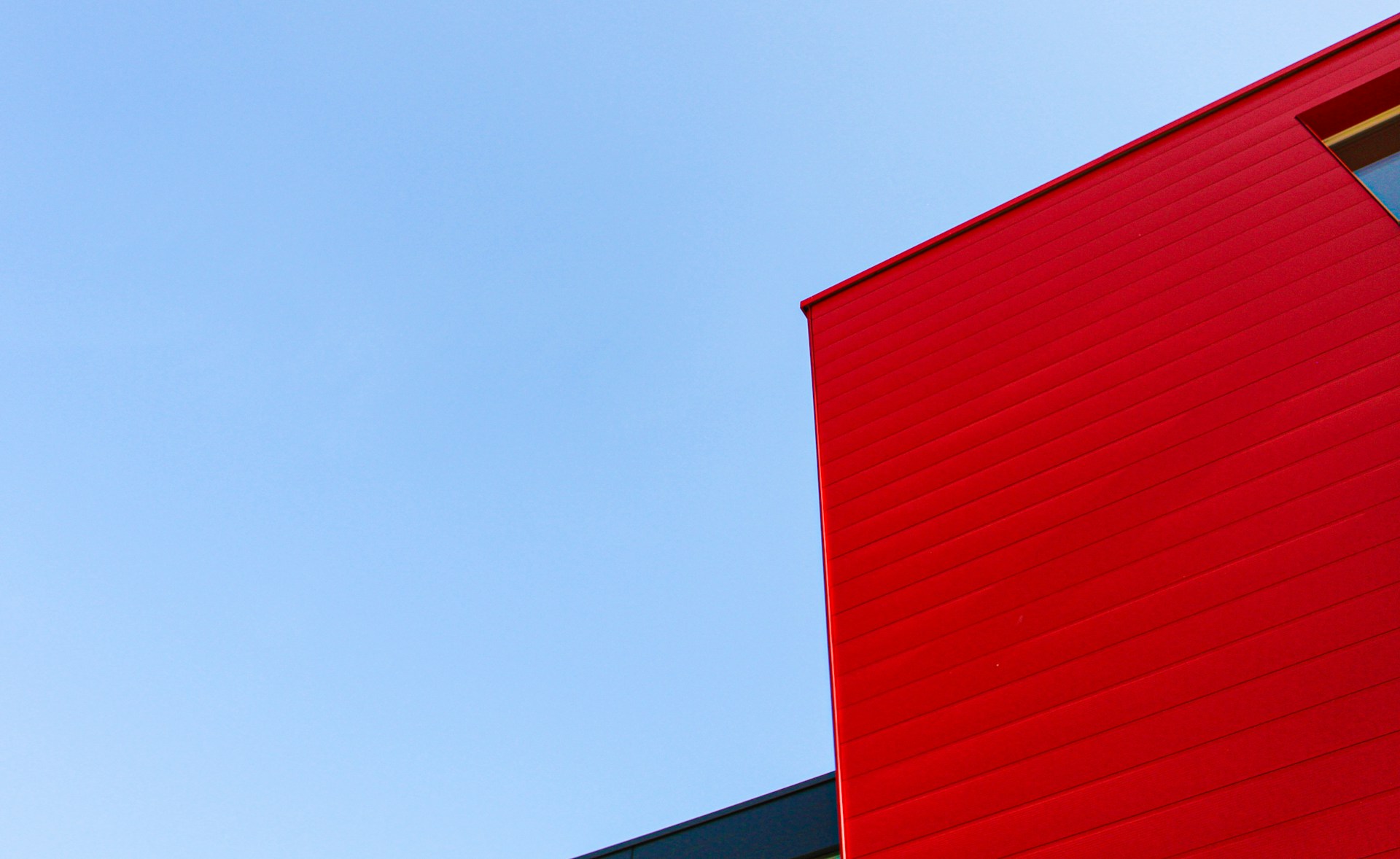 Colour photograph of a grey and red building against a blue sky