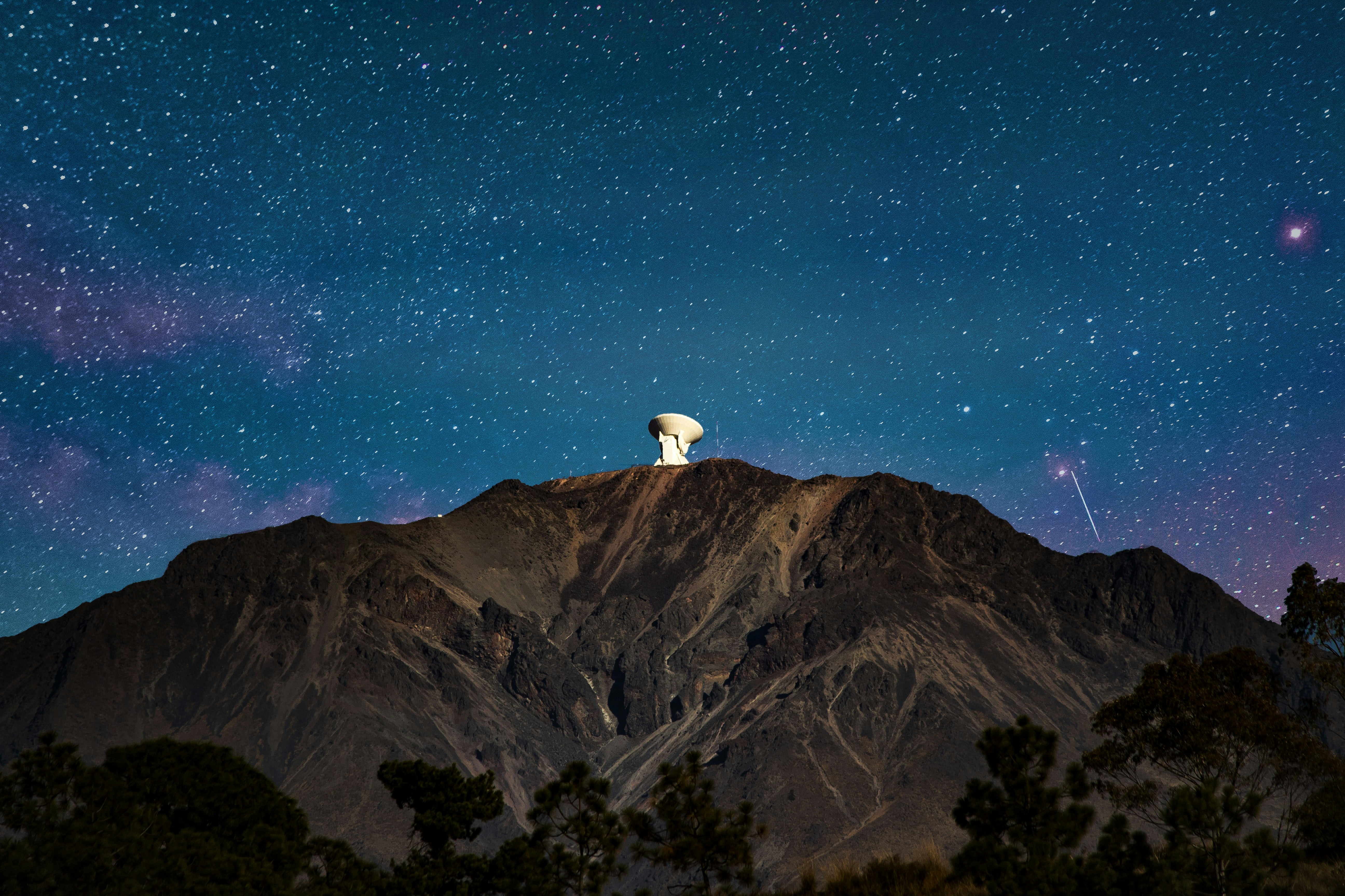 Radio telescope on a mountain under a star-filled night sky.