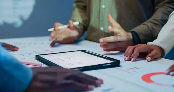 Hands collaborating around a tablet and documents during a meeting.