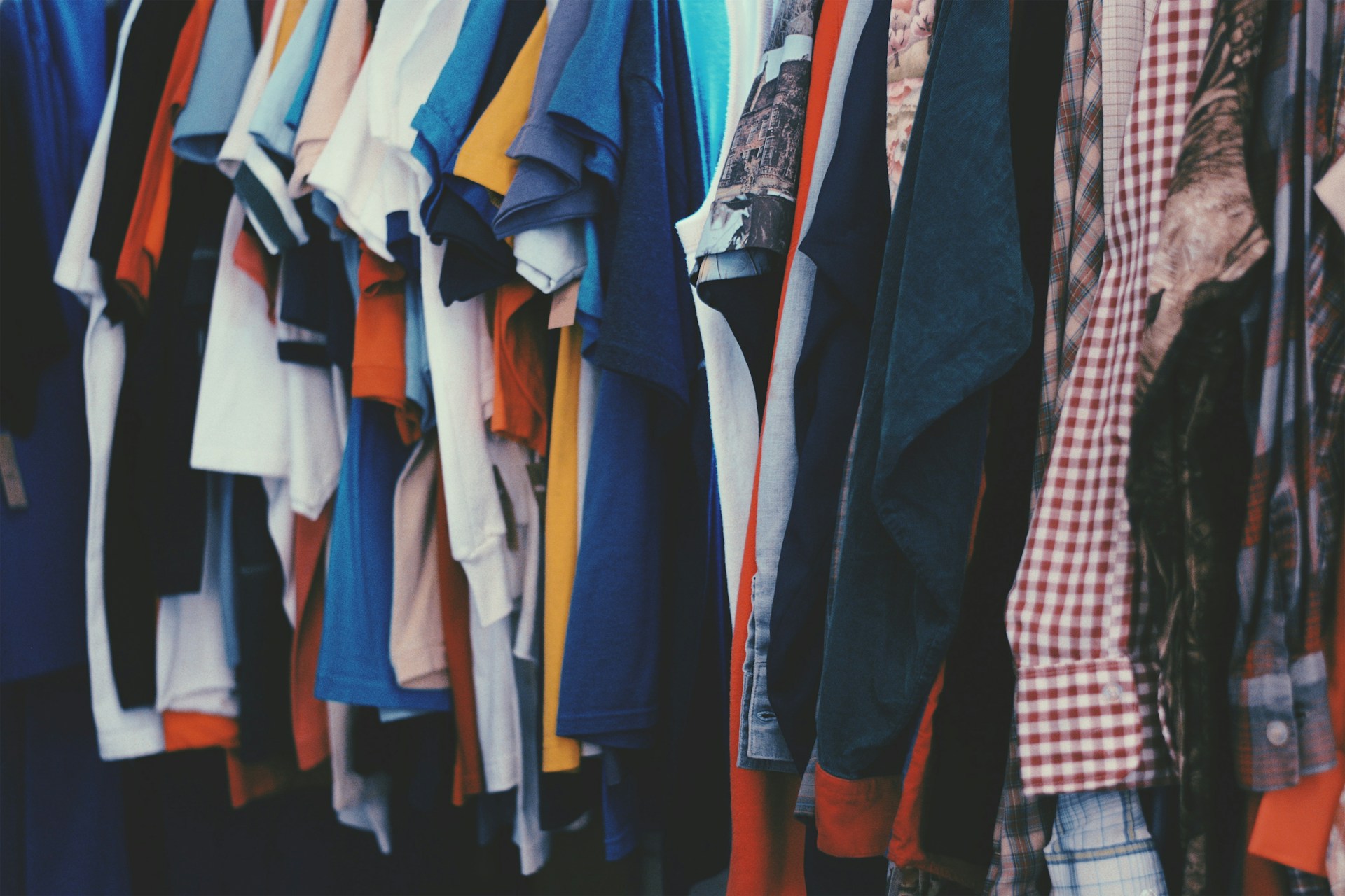 Clothes hanging on a rack, showing a variety of shirts and jackets in different colours and fabrics.
