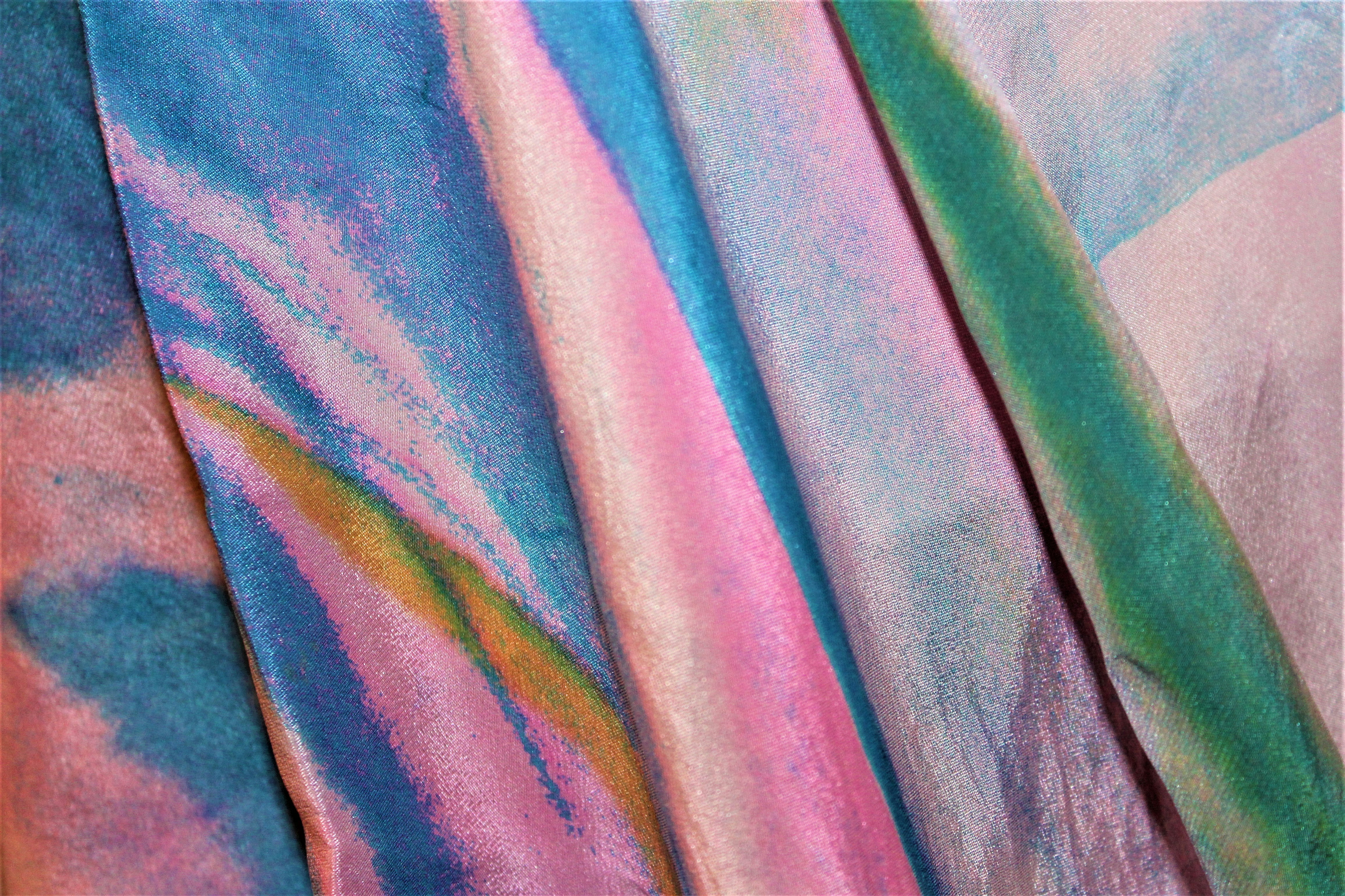 A close-up of fabric with soft folds  with pastel tones of pink, blue, green, and gold in a fluid, marbled pattern.