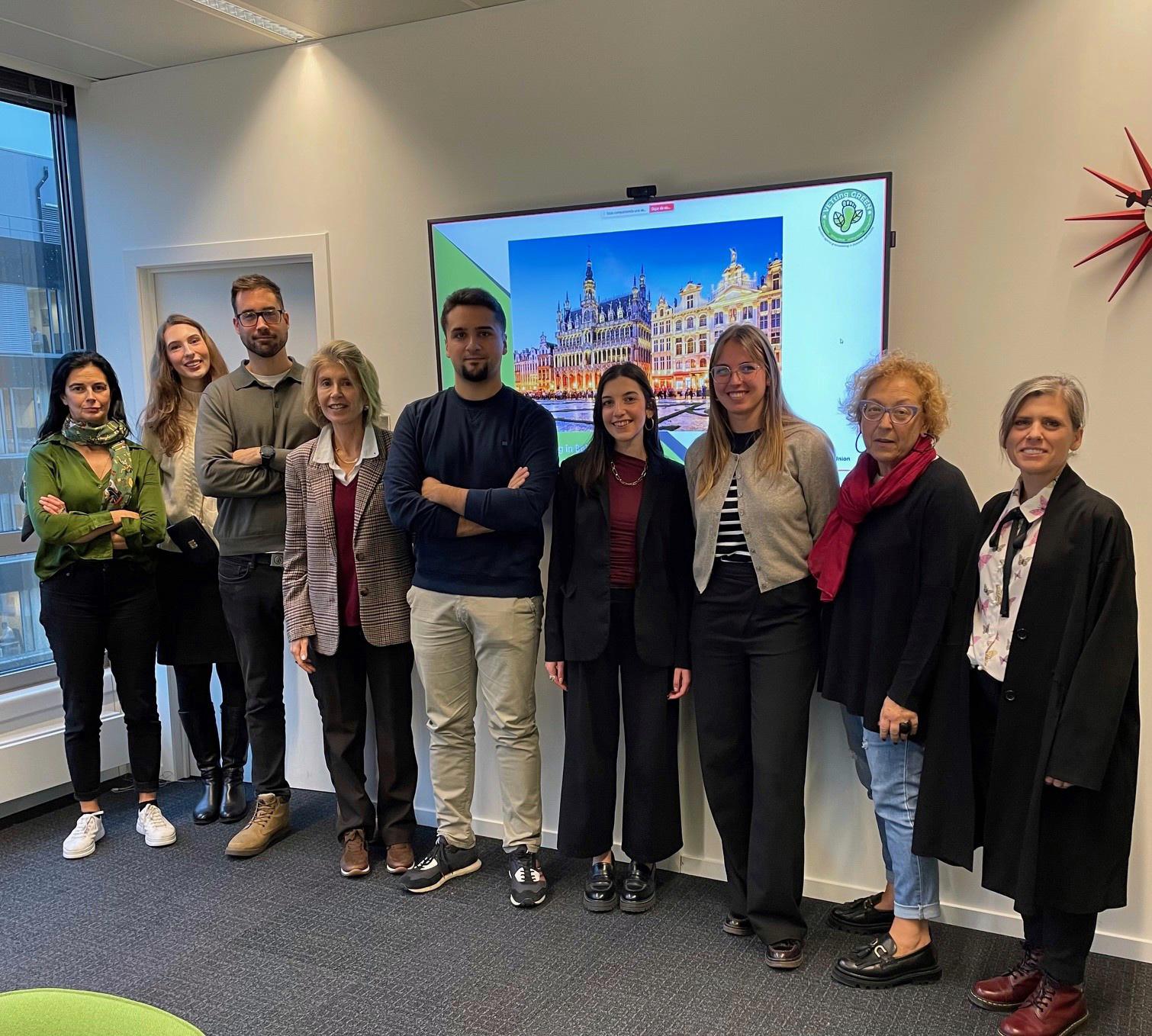 Colleagues posing together in an office or meeting room, standing in front of a screen.