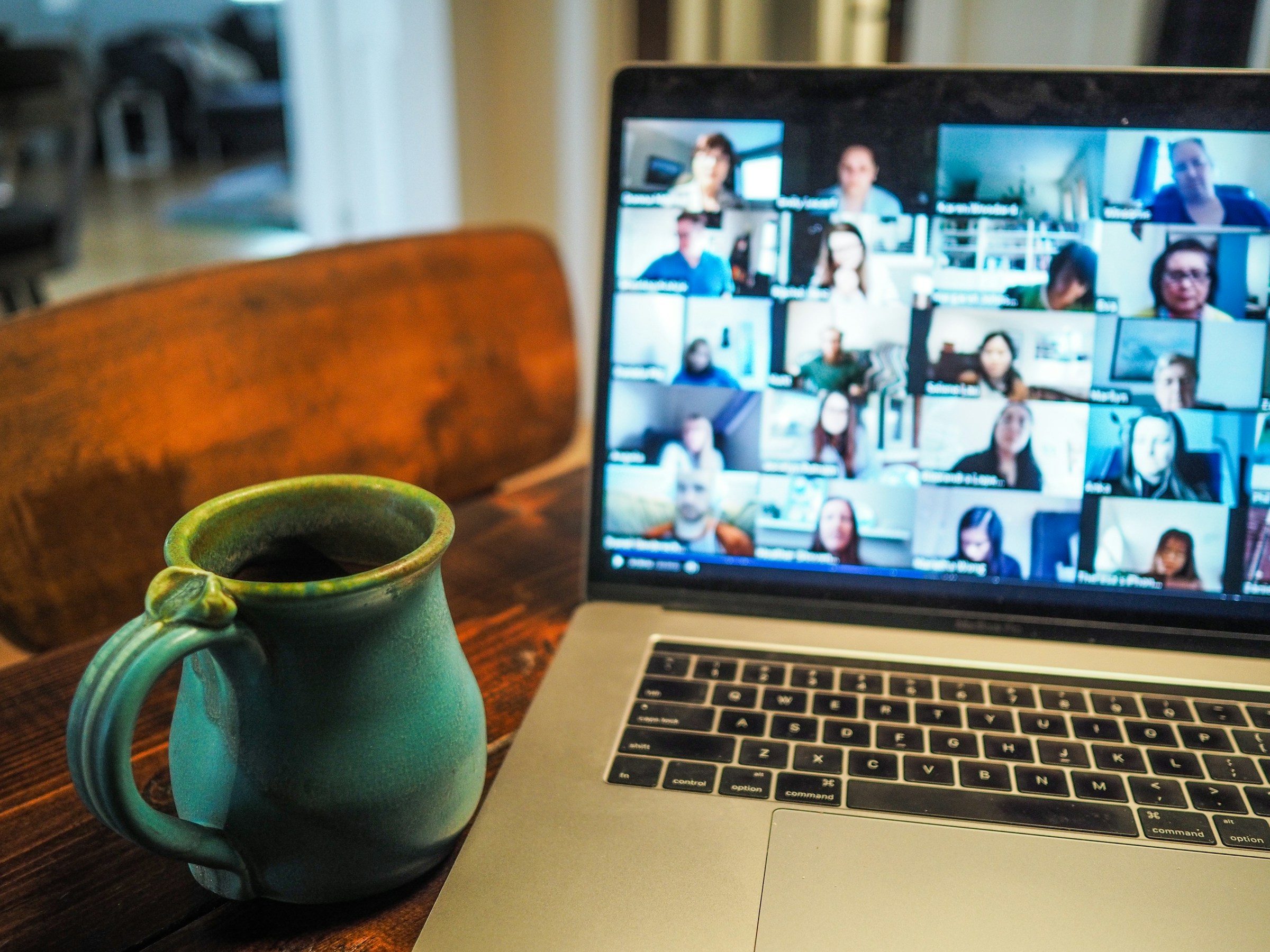 Laptop showing an online meeting with multiple participants, next to a ceramic mug.