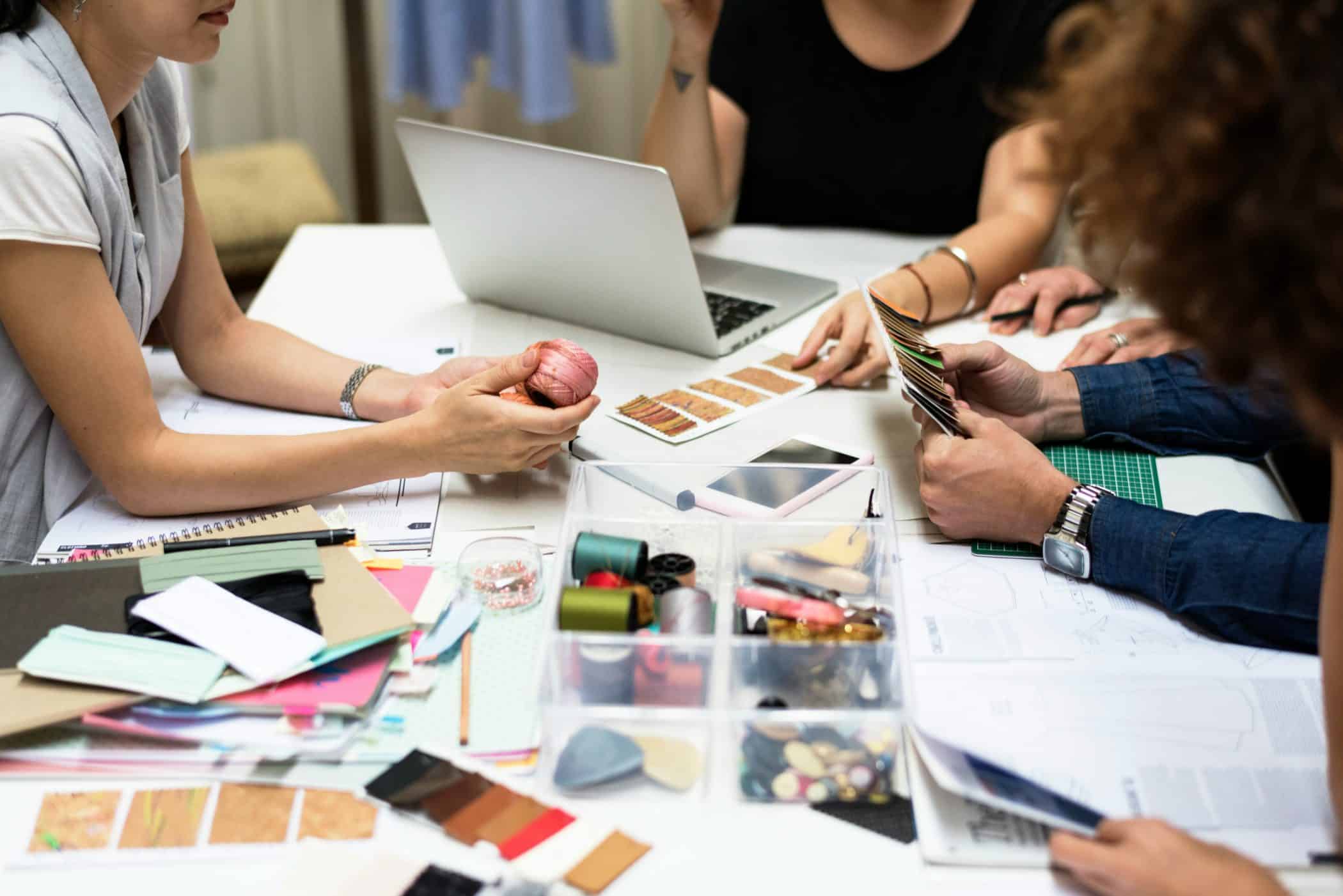 Group of people collaborating around a table, reviewing fabric samples, colour swatches, and materials with a laptop.