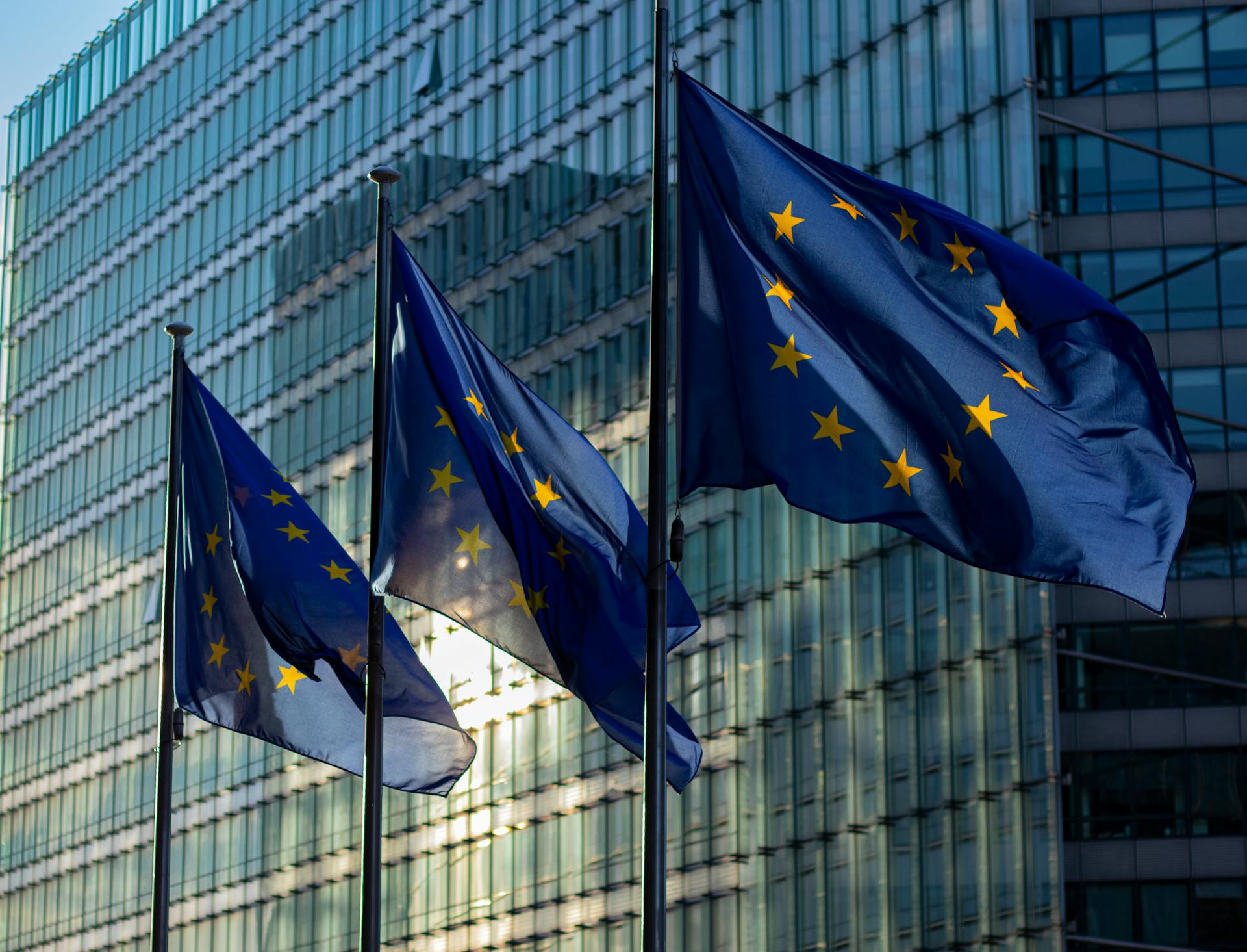 European Union flags flying in front of a modern glass office building.