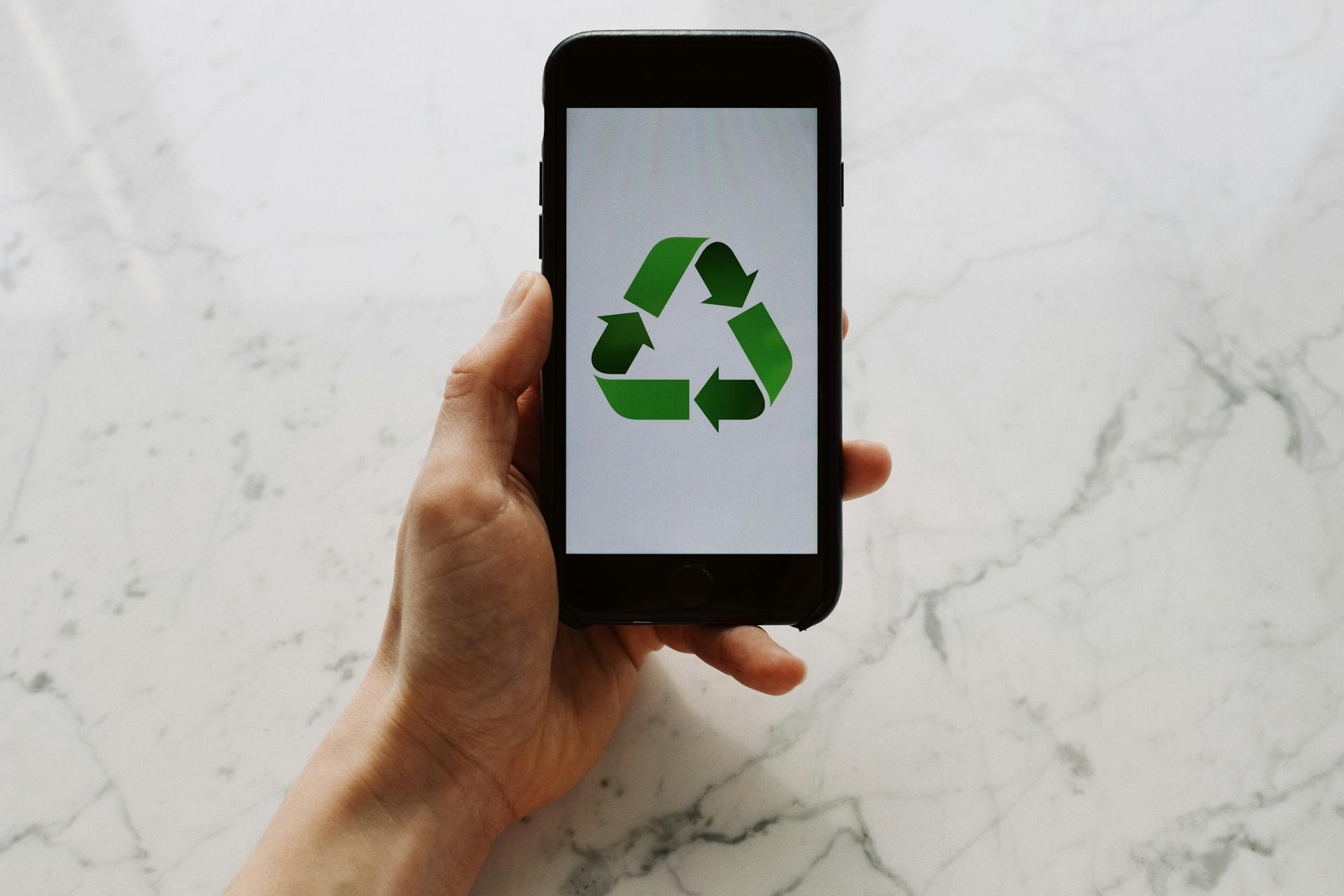 A hand holding a smartphone displaying a green recycling symbol.