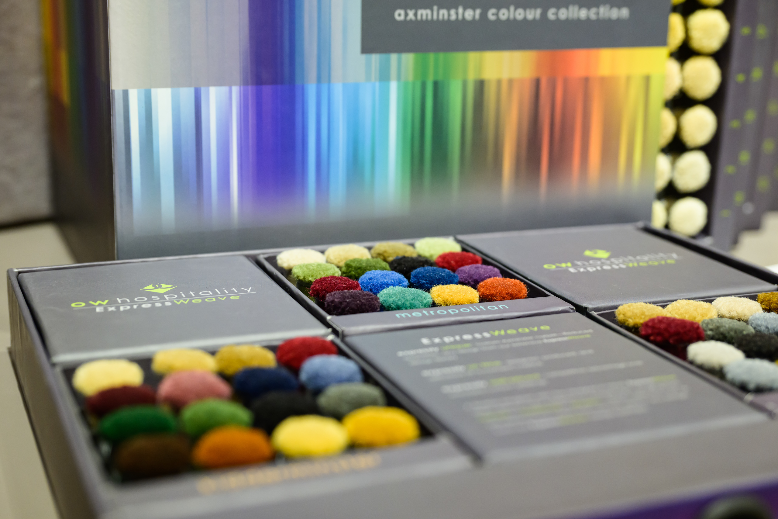 Display of colourful textile yarn pom-pom samples arranged in branded sample boxes.