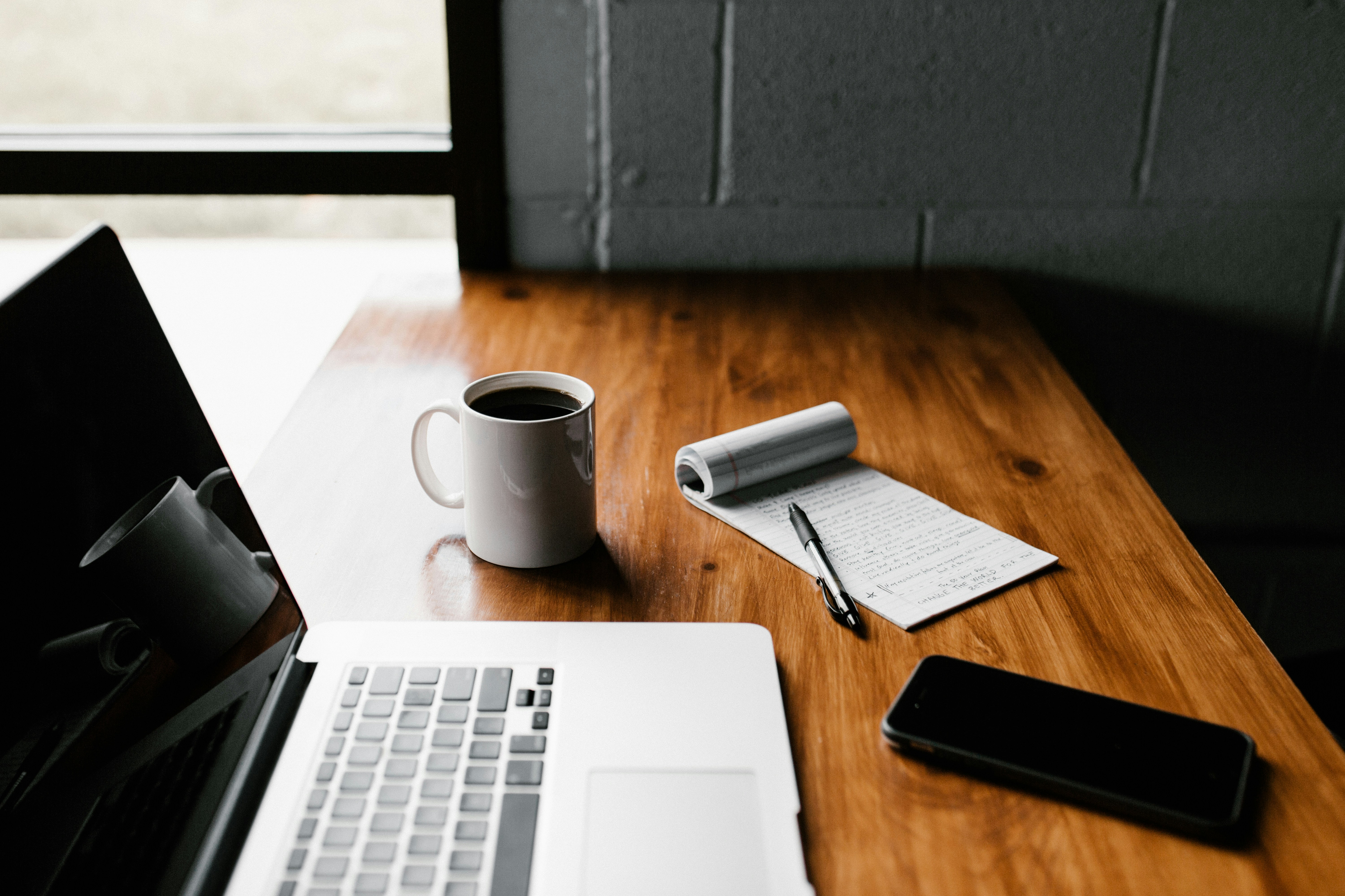 A laptop, cup of coffee and a notebook on a table