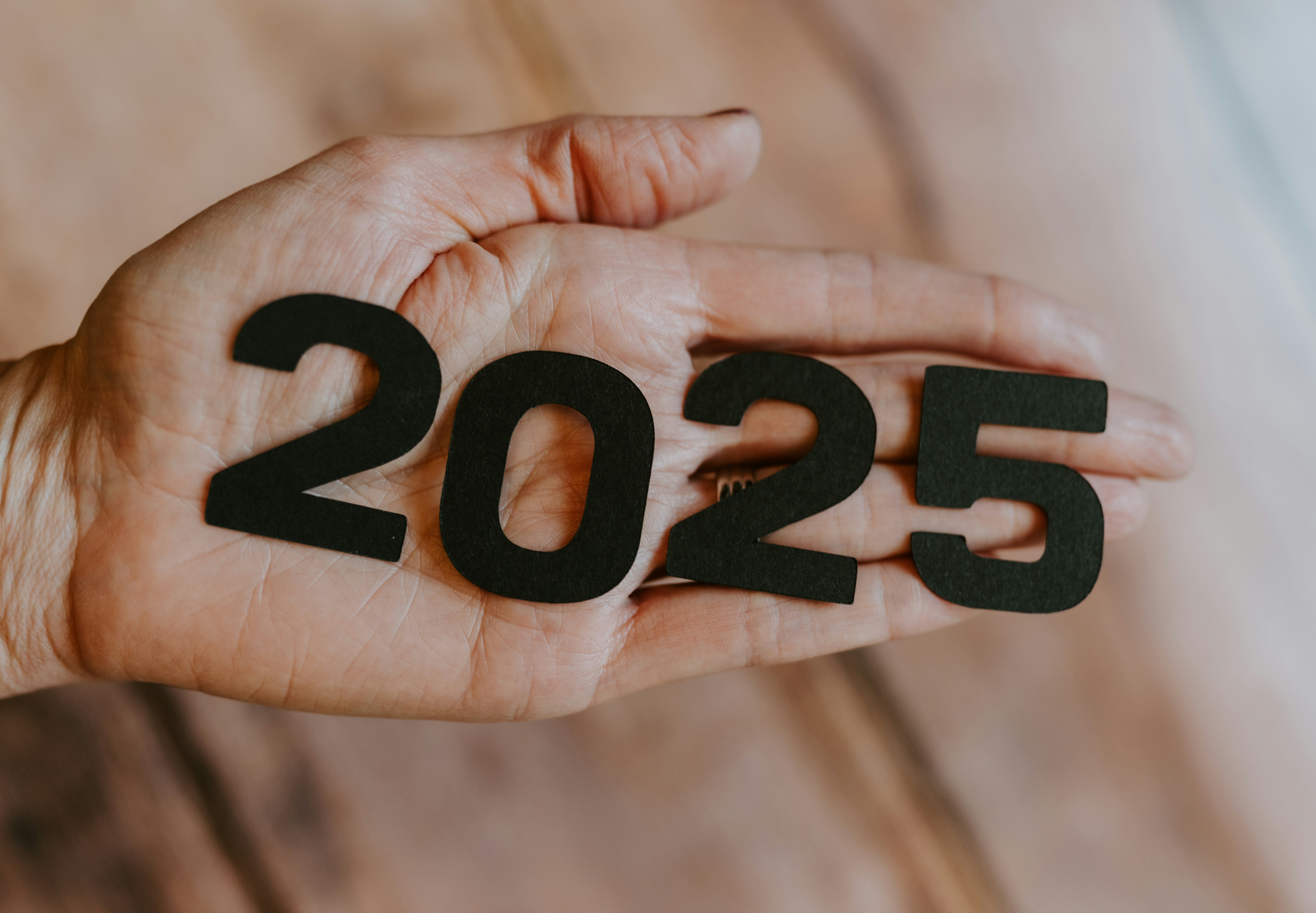 Hand holding the numbers ‘2025’ against a neutral background.