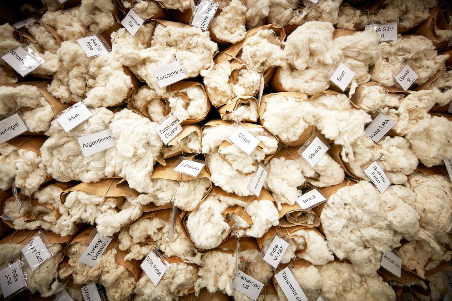 Stacked bundles of raw cotton labeled by country of origin.
