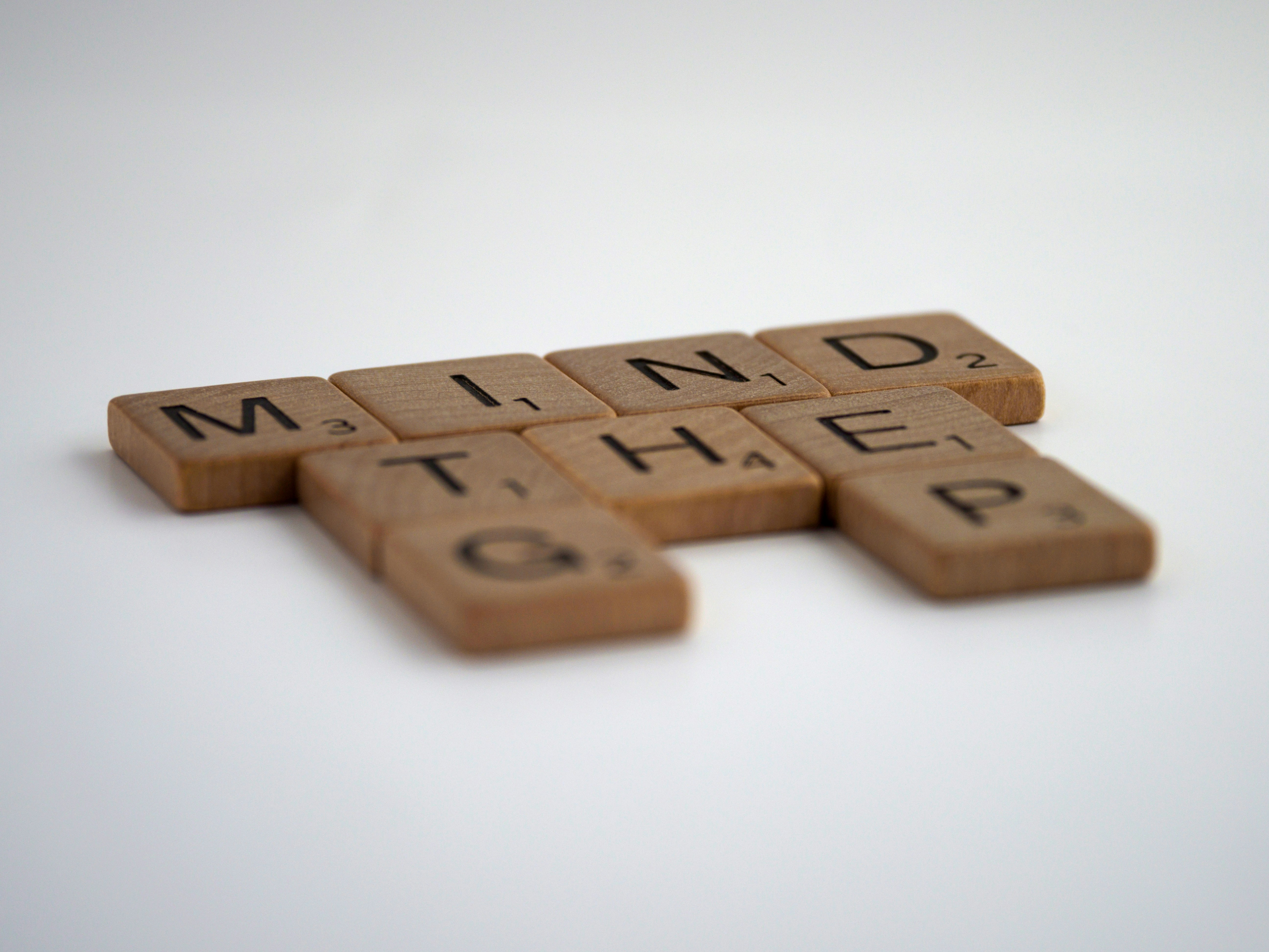 Colour photograph of brown wooden blocks spelling “Mind the G_P”, placed on a white surface. Photograph by Brett Jordan on unsplash.org