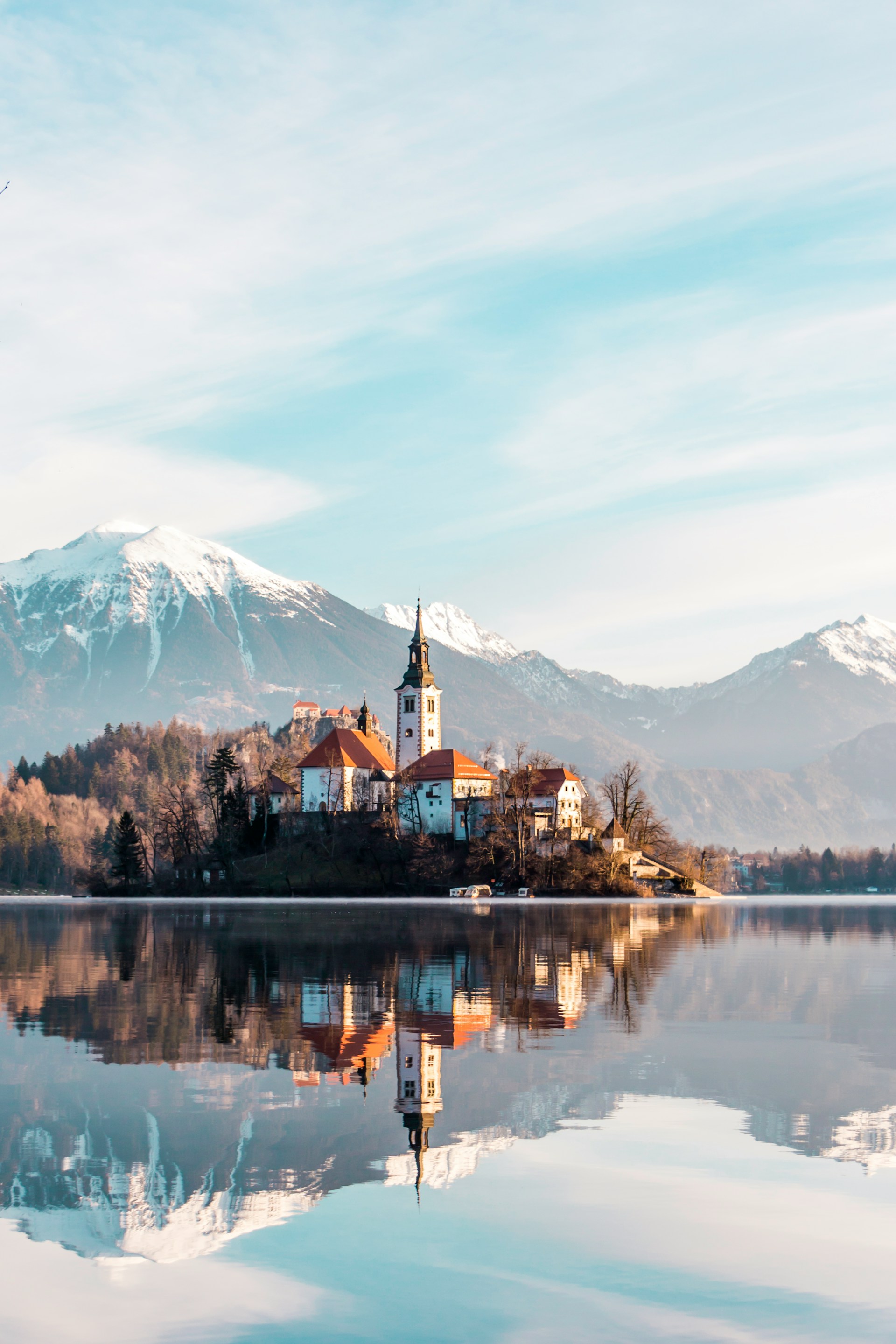 brown-and-white-concrete-building-near-body-of-water-and-mountain-under-white-clouds-and-blue