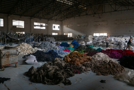 Sorted piles of colourful fabric waste inside a large industrial warehouse.