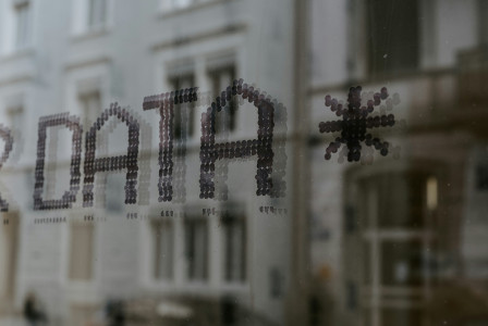 Window with the word “DATA” in dotted lettering, reflected over a blurred street scene.