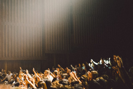People raising their hands inside auditorium.
