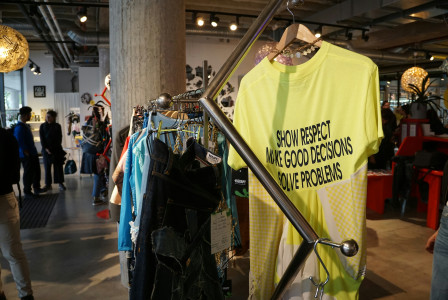 Clothing rack in a modern shop displaying a bright yellow T-shirt with the slogan “Show Respect Make Good Decisions Solve Problems.”