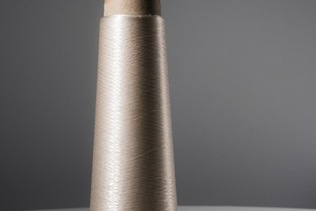 Spool of translucent thread on a cardboard cone with a gray background.