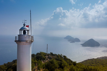 white-and-brown-lighthouse-near-green-trees-under-white-clouds-and-blue-sky