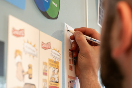 Person writing notes on a wall with diagrams and printed materials.
