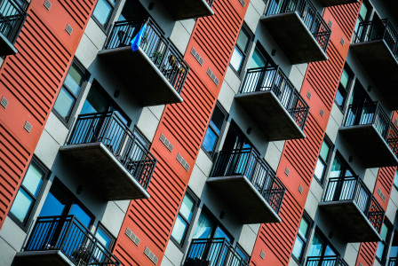 The image shows the exterior of a modern apartment building with multiple balconies.