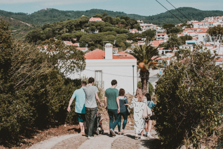 A group of people strolling down a path in a charming European village with lush greenery.