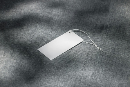 Blank clothing tag resting on a grey textile fabric surface.