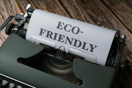 Photo presenting a vintage green typewriter on a wooden surface, with a sheet of paper rolled into it reading "ECO-FRIENDLY" in bold typed letters.