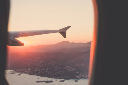 A picture presents an airplane wing above the landscape at sunset.