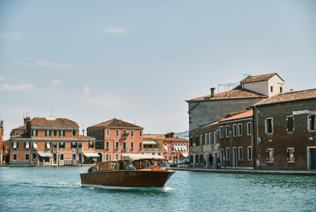 A picture presents a boat traveling along a canal beside historic buildings.