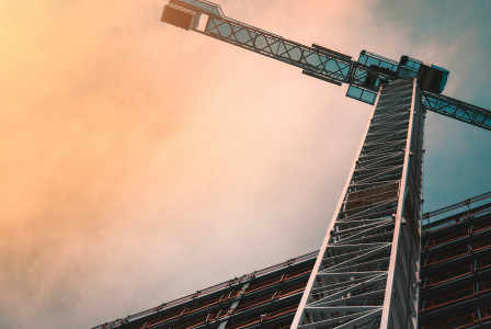 A photo presents a construction crane beside a tall building.