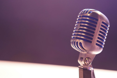 Photo presenting a vintage microphone on a stand against a blurred purple background.
