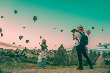 A photo of two tourists watching hot air balloons over a rocky landscape.