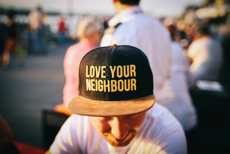 A photo presents a person wearing a “Love Your Neighbour” cap.