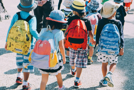 A picture presents children walking outdoors with backpacks