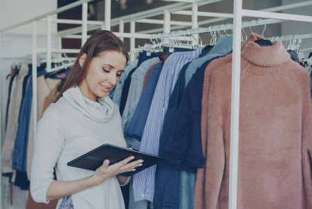 woman holding a tablet while standing next to hung clothes