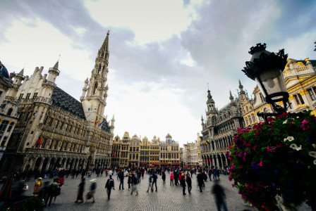 A picture presents a historic city square with grand buildings and people.