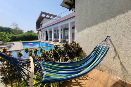 The picture presents a colorful hammock beside a swimming pool at a modern house.