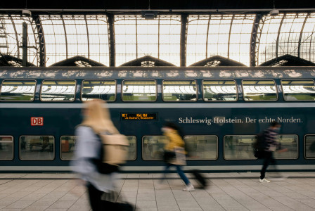 The photo presents people walking past a train at a station.