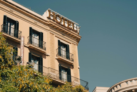The photo presents the exterior of a hotel building with balconies and a rooftop hotel sign.